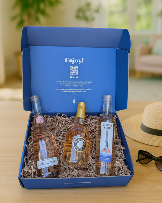 Three bottles of Rosé wine in a blue gift box with 'Enjoy!' text, placed on a wooden surface.